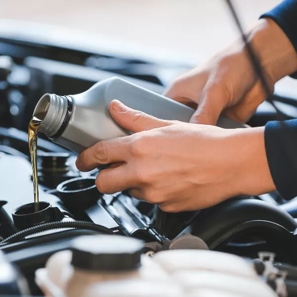 Close-up of hands pouring engine oil from a gray bottle into a cars engine under the hood.