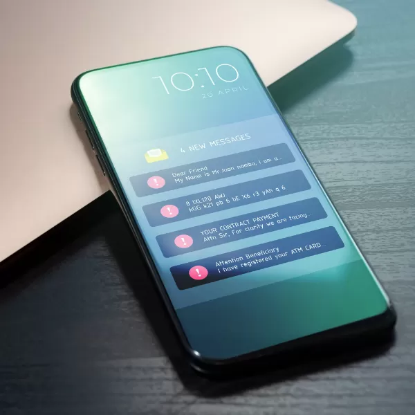 A smartphone on a table displays multiple notifications for new messages and alerts on its screen, next to a closed laptop.