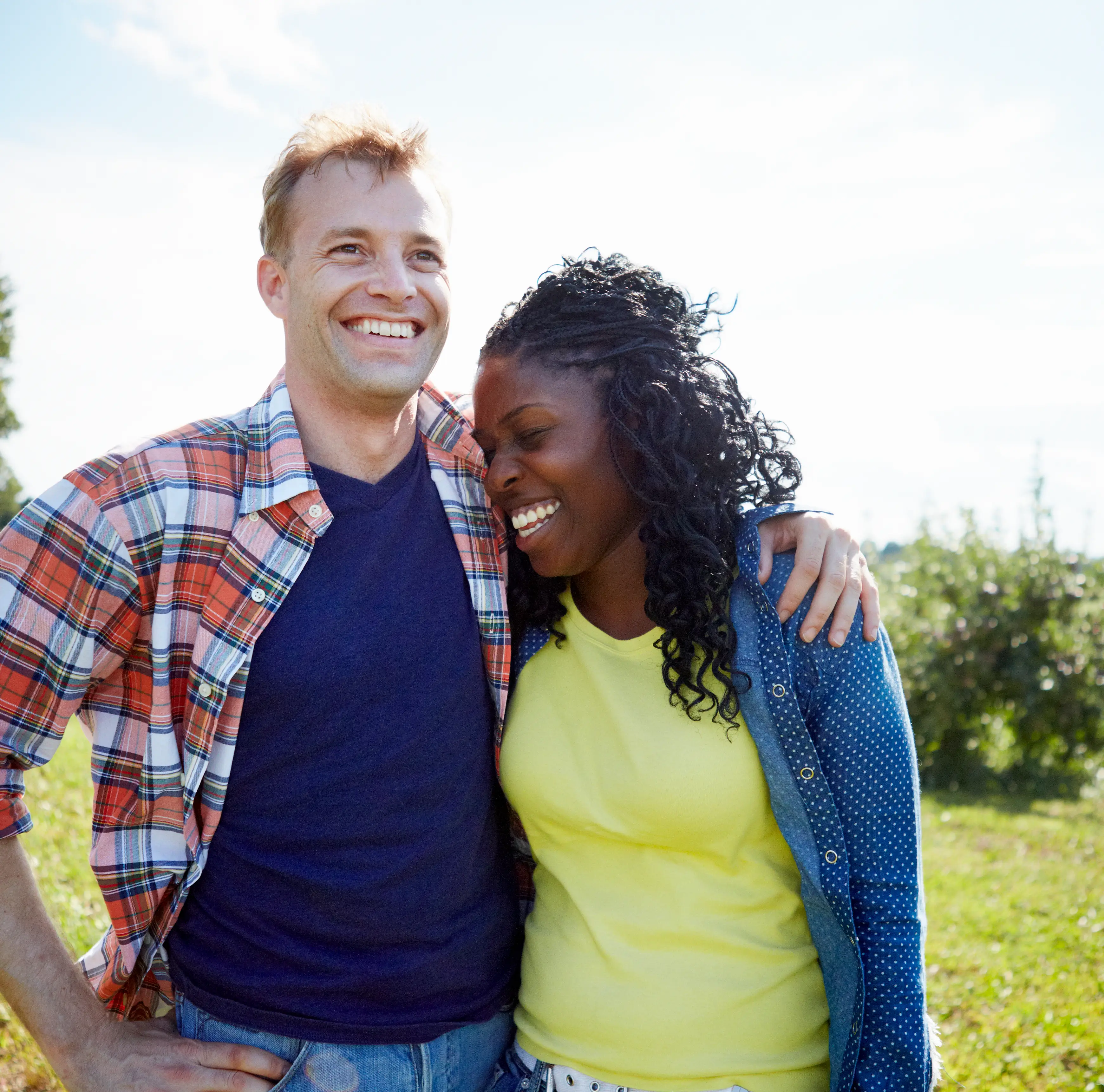A man and woman smiling and standing close together outdoors, with the man’s arm around the woman’s shoulders on a sunny day, celebrating recent sponsorships.