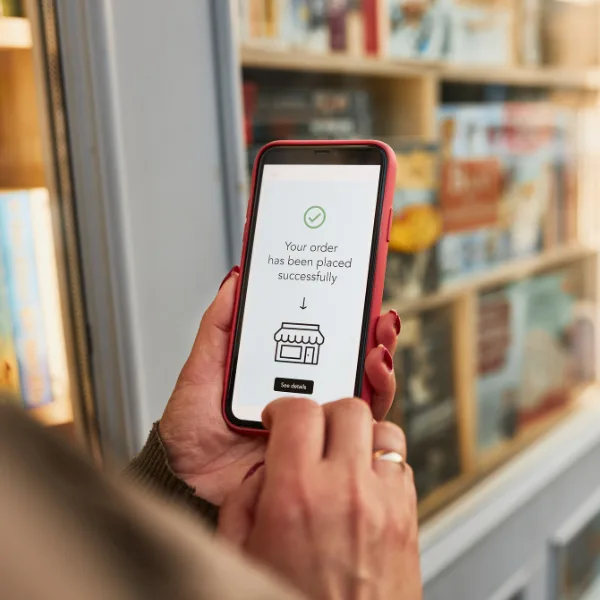 A person holding a smartphone with a screen showing Your order has been placed successfully in front of shelves filled with books.
